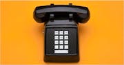 An old-style push-button landline telephone, against a yellow background.