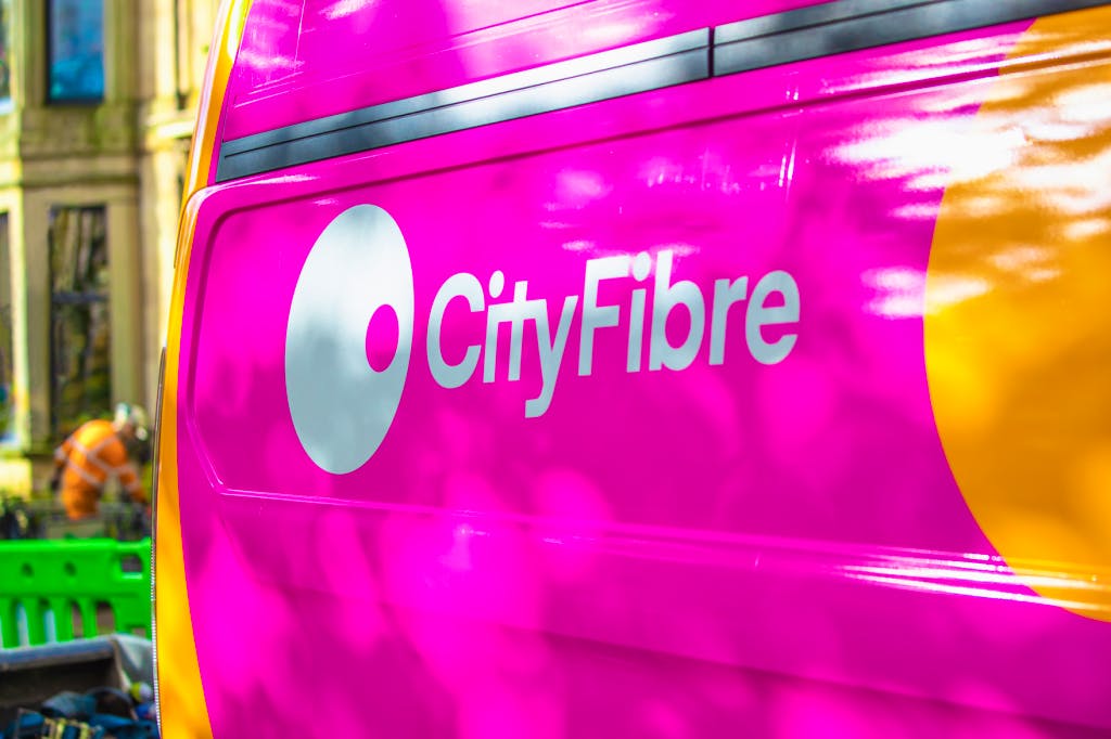 A CityFibre workmans van parked outside some houses, with an engineer blurrily working in the background.