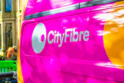 A CityFibre workmans van parked outside some houses, with an engineer blurrily working in the background.